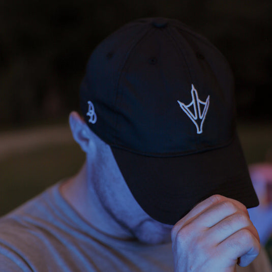 A man wearing a black baseball cap with a white stylized logo and a gray t-shirt, photographed in low-light outdoor conditions with a blue cast.